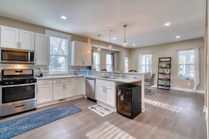 A modern kitchen with white cabinets, stainless steel appliances, and pendant lighting.