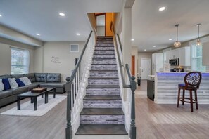 A staircase leading to a second floor, a living room with a sofa and coffee table, and a kitchen area with a bar.