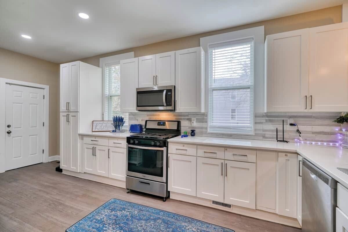 A modern kitchen with white cabinets, stainless steel appliances, and a blue rug.