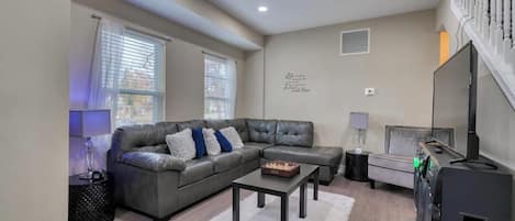 A living room with a sectional sofa, a coffee table, a flat-screen TV, and a staircase.