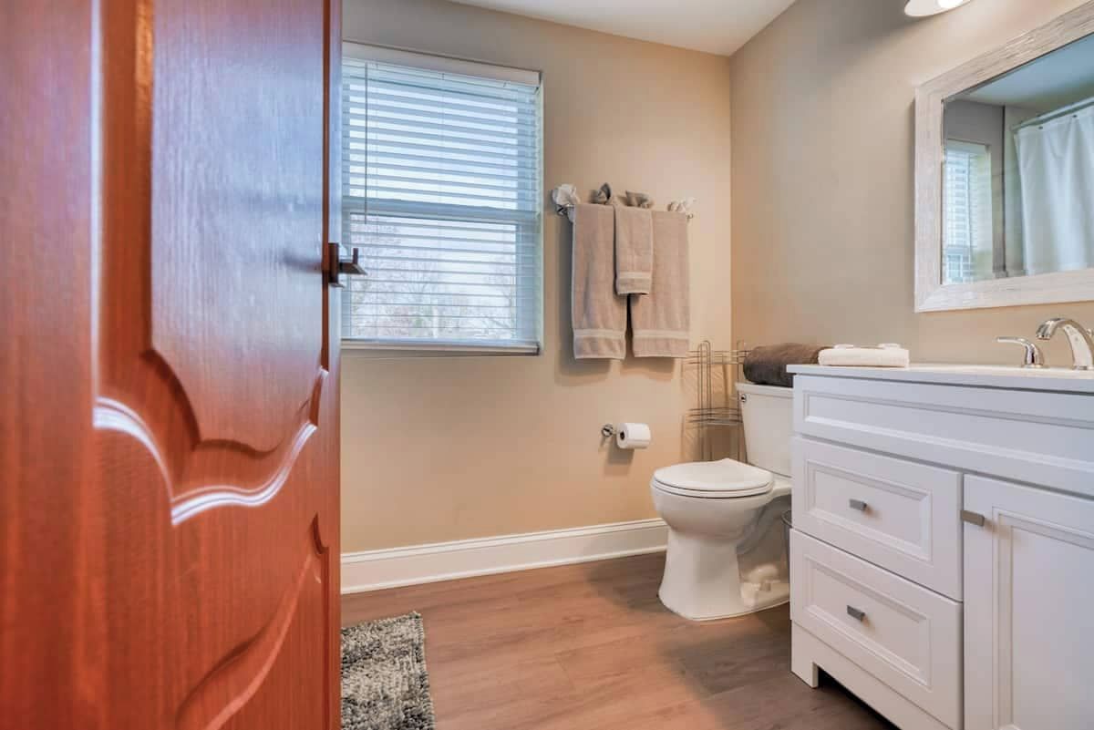 A bathroom with a toilet, a sink, a mirror, and a window with blinds.