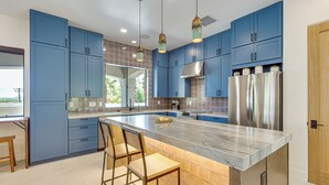 A kitchen with blue cabinets, a marble island, stainless steel appliances, and hanging pendant lights.