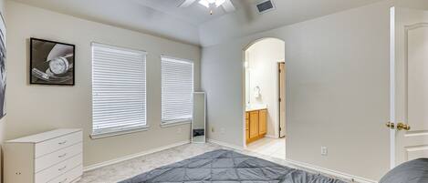 A bedroom with a bed, ceiling fan, dresser, and two windows with blinds.