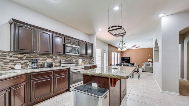 A modern kitchen with dark wood cabinets, a granite countertop, and a stainless steel refrigerator. - Private Theater & Pool: Spacious Mission Home (Mission)
