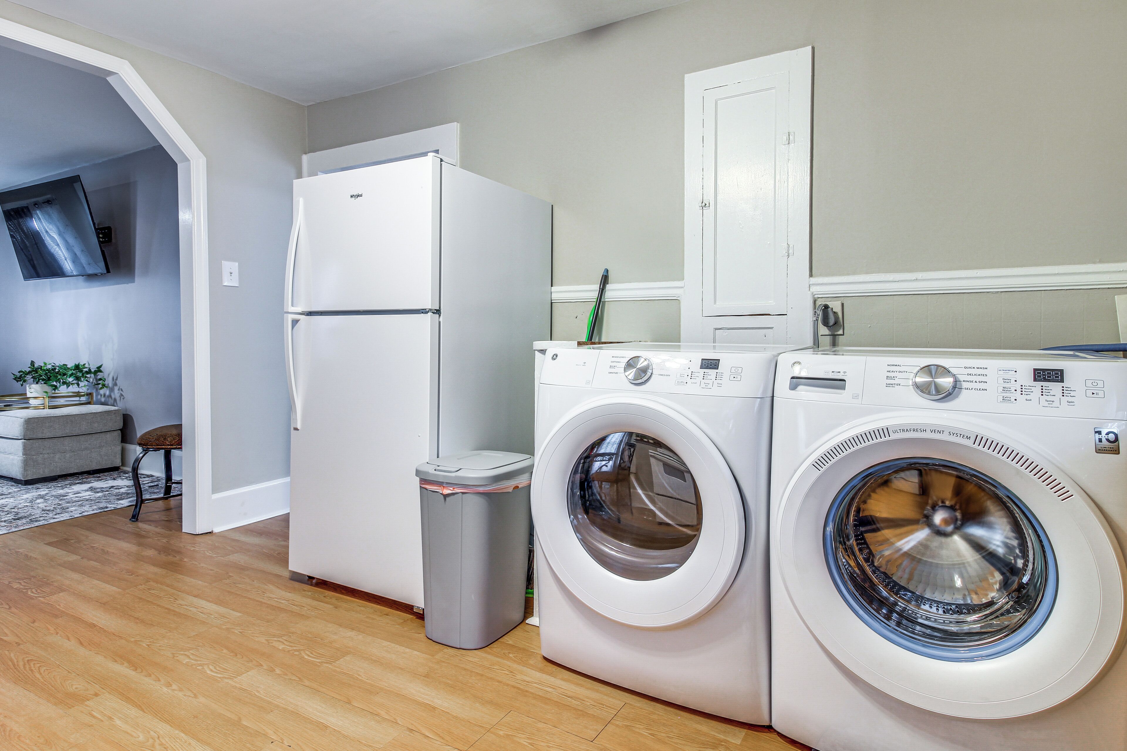 A laundry room with a washing machine and dryer, a trash can, and a refrigerator.