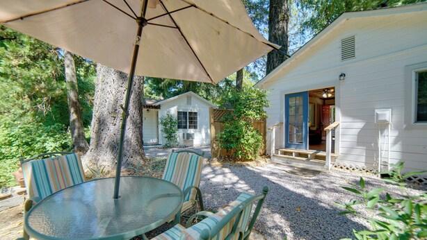 Une terrasse avec une table ronde et des chaises à rayures, un parasol beige et une maison mobile blanche dotée d’un porche.