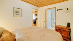 Une chambre avec un plafond en bois, un lit avec des oreillers, une commode et une porte donnant sur la cuisine.