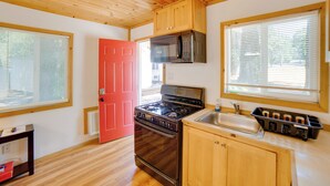 Une cuisine de taille réduite, avec des meubles en bois, une porte rouge, une cuisinière, un four à micro-ondes et un évier.
