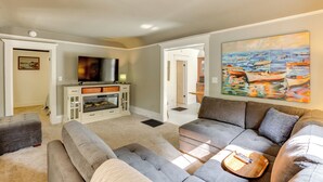 A living room with a gray sectional sofa, a flat-screen TV, and a painting of boats on the wall. - Home Close to Downtown Frankfort, Walk to Beach! (Frankfort)