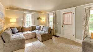 A living room with a sectional sofa, a lamp, and a door with curtains. - Home Close to Downtown Frankfort, Walk to Beach! (Frankfort)