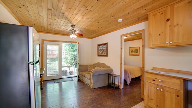 A room with wooden flooring, a sofa, a cabinet, and a door leading to a balcony. - Golf & Hike: Cobb Mountain Cabin in Scenic Forest! (Cobb)
