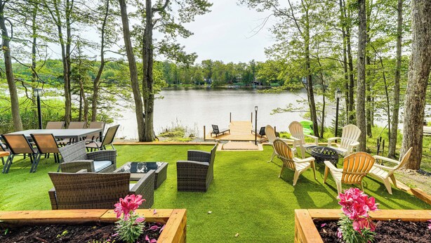 A lakeside patio with outdoor furniture and a wooden deck overlooking the water. - Hot Tub + Game Room! Lakefront Gem in Pocono Mtns (Tobyhanna)
