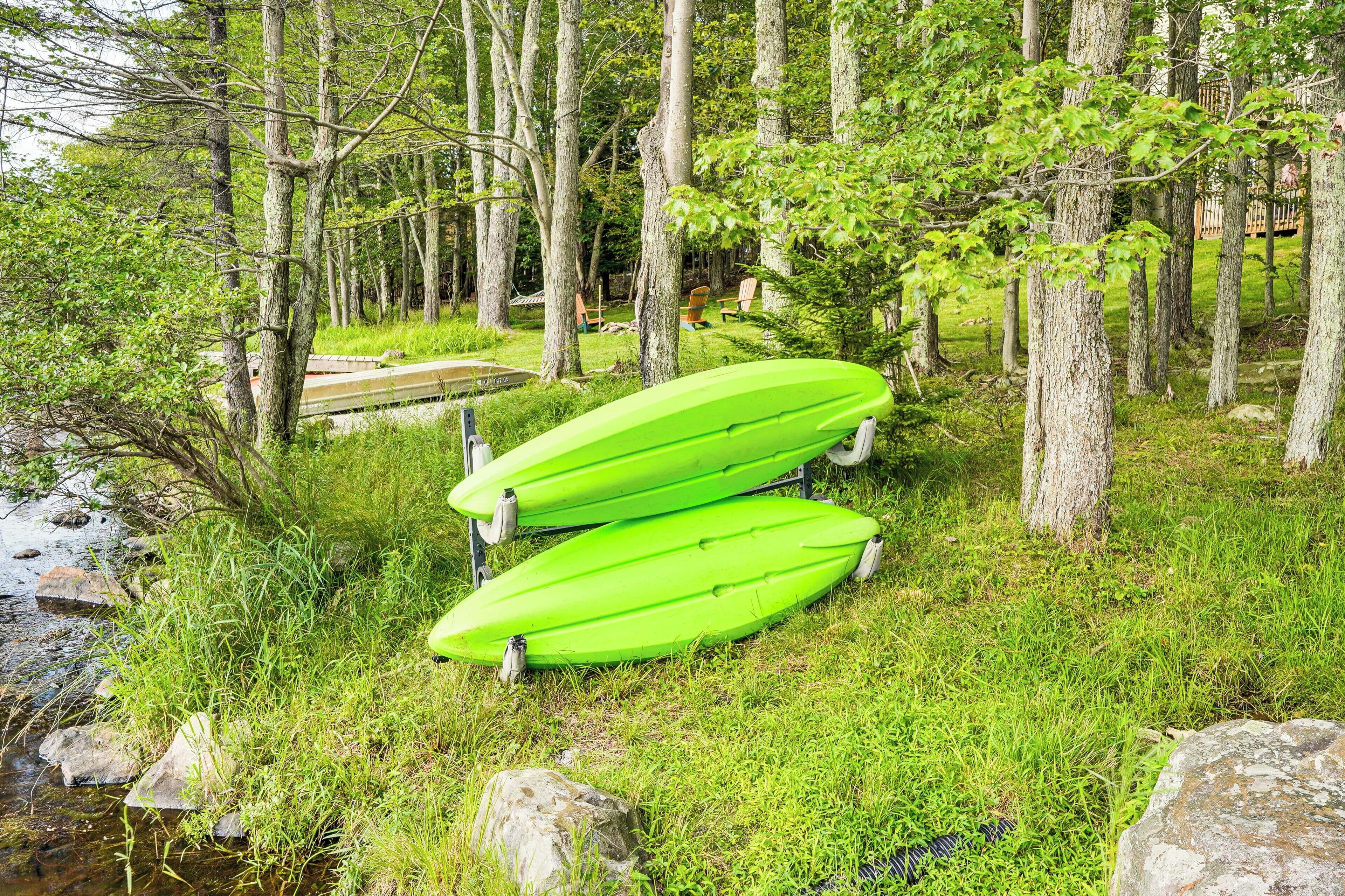 Zwei grüne Kajaks auf einer Wiese nahe eines Flusses, umgeben von Bäumen.