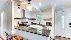 A modern kitchen with granite countertops, a central island with bar stools, stainless steel appliances, and pendant lighting. - Hot Tub + Game Room! Lakefront Gem in Pocono Mtns (Tobyhanna)
