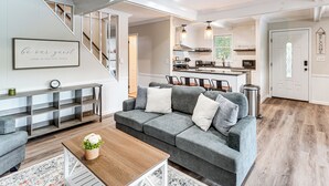 A modern living room with a grey sectional sofa, wooden coffee table, and a staircase leading to a kitchen area. - Hot Tub + Game Room! Lakefront Gem in Pocono Mtns (Tobyhanna)
