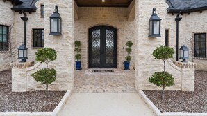 A stone building with a large arched entrance, black double doors, and potted plants on either side. - Breathtaking 4 bedroom home within the golf-course community of Canyon West. (Weatherford)