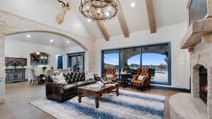 A spacious living room with a fireplace, leather sofa, and a chandelier. - Breathtaking 4 bedroom home within the golf-course community of Canyon West. (Weatherford)