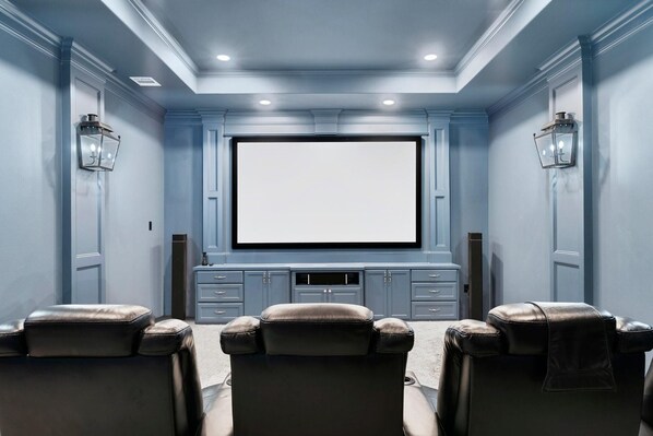 Un cine en casa con una pantalla grande, sillones de cuero reclinables y altavoces empotrados.
