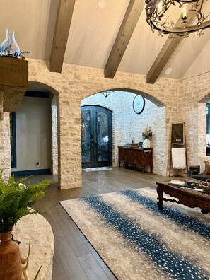 A spacious room with a stone wall, a large wooden door, a chandelier, and a round clock.