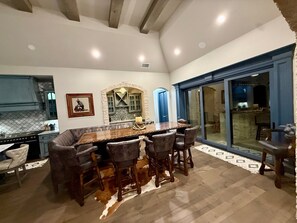 Uma sala de jantar com uma grande mesa de madeira, cadeiras de couro, lareira de pedra e vista através de portas de vidro.