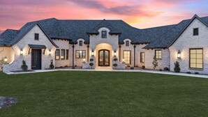 A large stone house with a symmetrical facade, multiple windows, and a well-maintained lawn. - Breathtaking 4 bedroom home within the golf-course community of Canyon West. (Weatherford)
