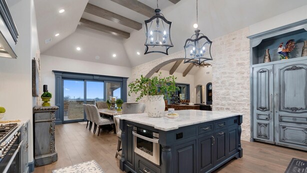 A spacious kitchen with dark cabinetry, a large island, and hanging pendant lights. - Breathtaking 4 bedroom home within the golf-course community of Canyon West. (Weatherford)