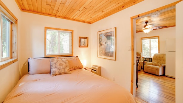 Un dormitorio con una cama grande, techo de madera, obras de arte enmarcadas y vistas al salón.