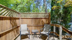 Terraza de madera con dos sillas y una mesa pequeña, rodeada de un cerco de madera y árboles.