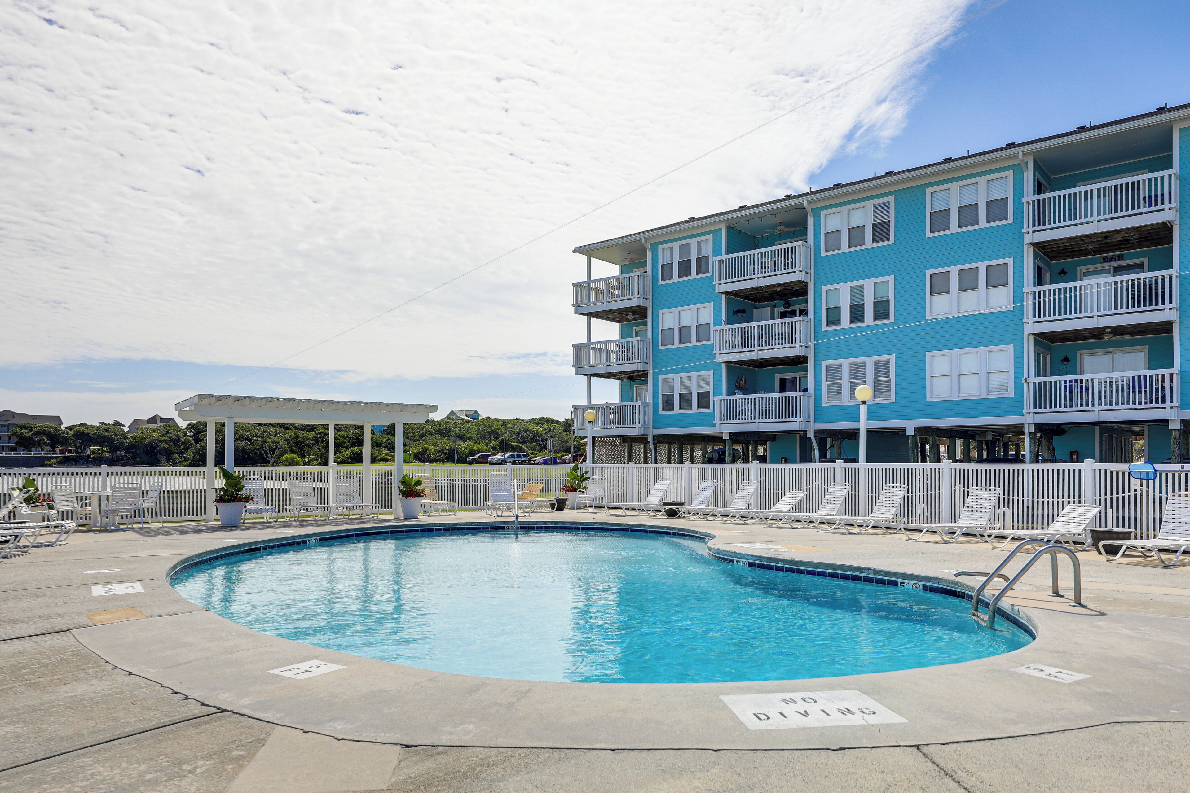 A swimming pool with lounge chairs and a building with balconies.