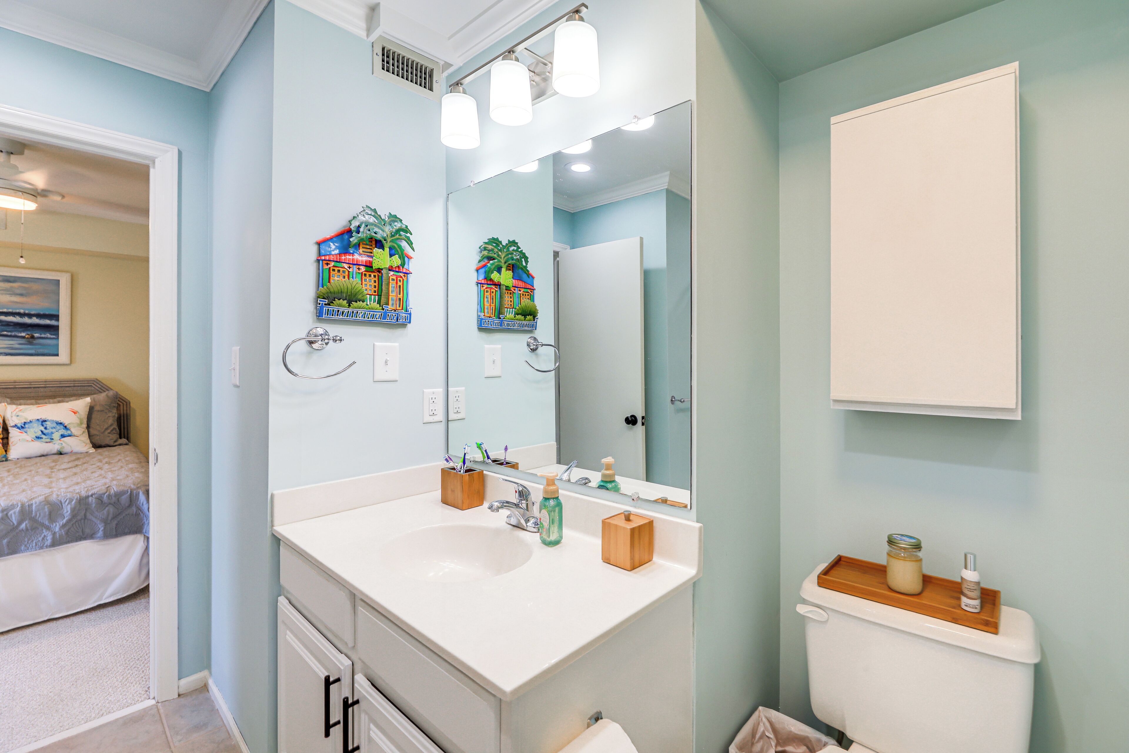 Une salle de bain avec un lavabo blanc, un miroir et des toilettes. On y trouve des brosses à dents et un distributeur de savon sur le lavabo.