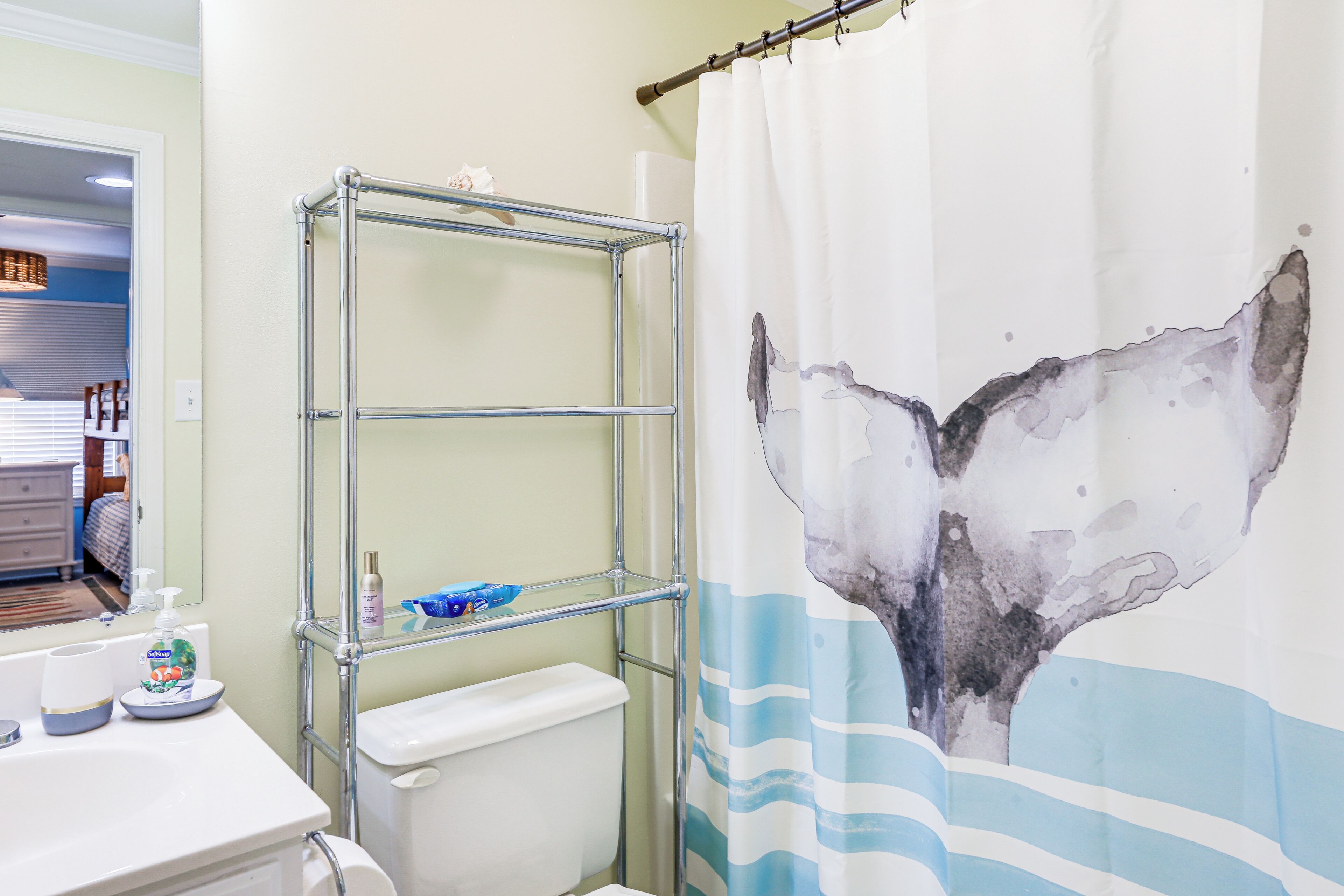 A bathroom with a shower curtain featuring a whale tail design, a metal shelving unit, and a toilet.