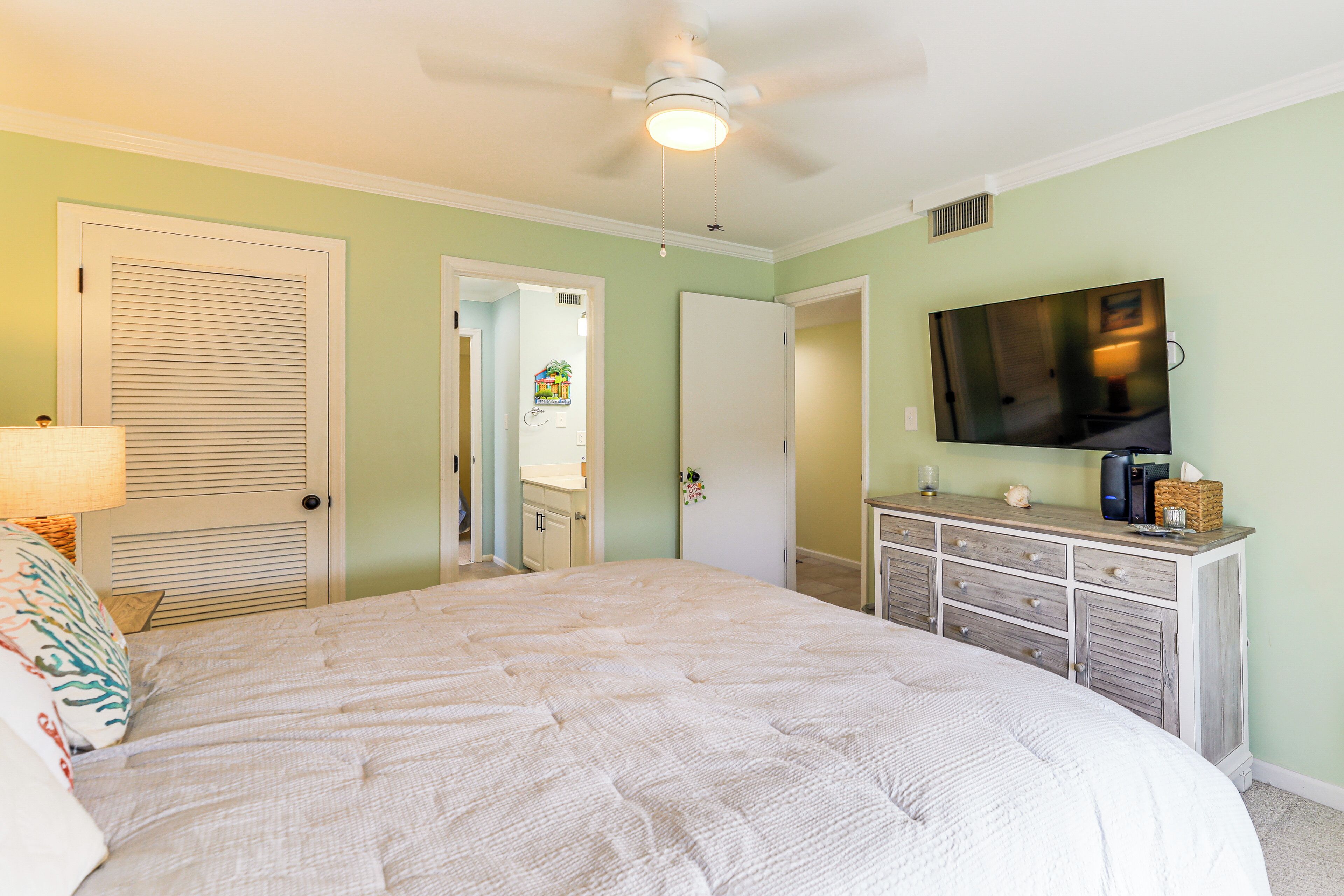 A bedroom with a large bed, a ceiling fan, a TV, and a dresser.