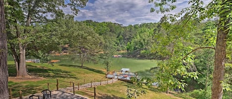 A lakeside outdoor seating area with chairs and a fire pit, surrounded by trees and a view of a lake and dock.