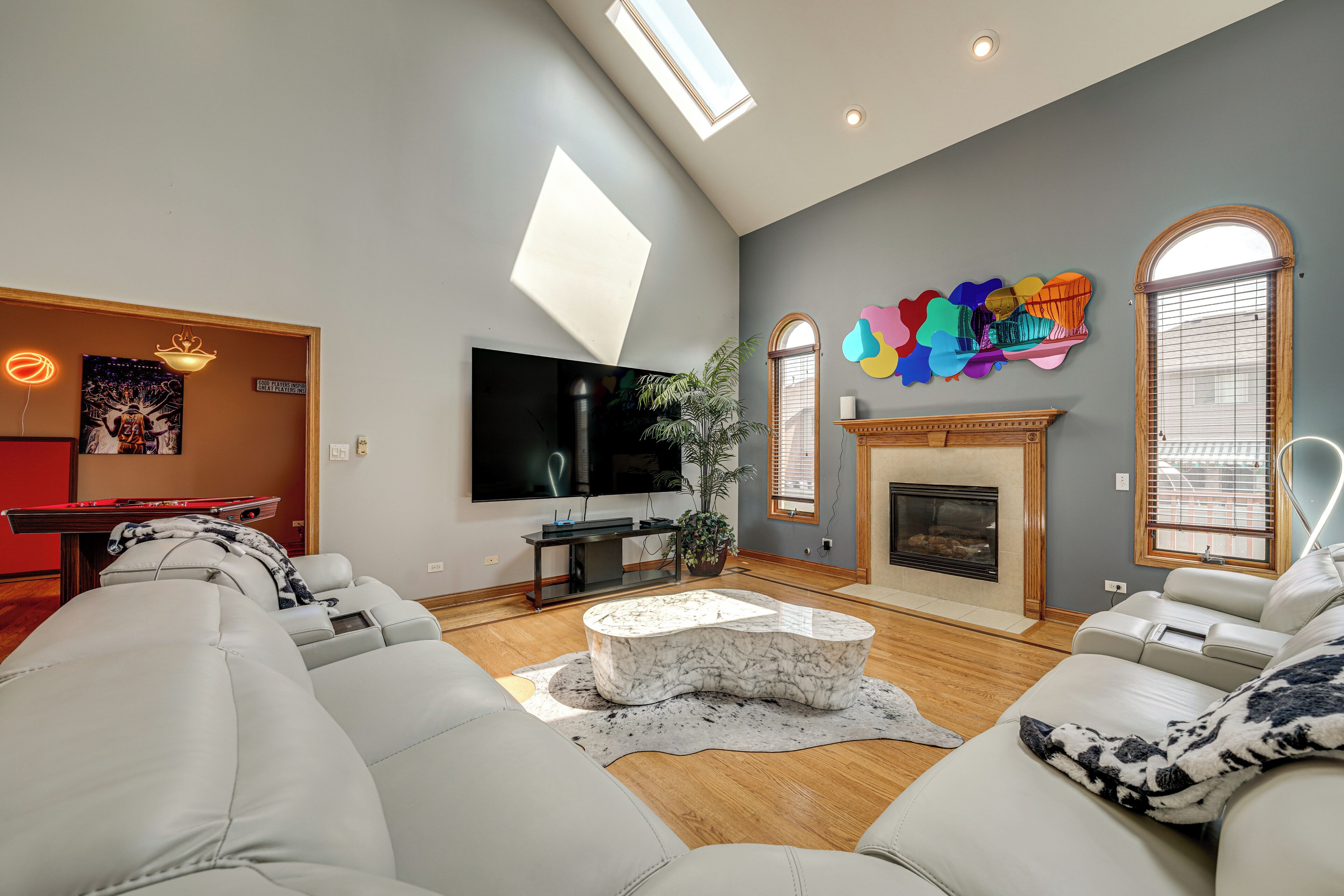 A modern living room with a large TV, comfortable seating, a fireplace, and a unique wall art piece.