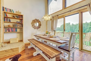 Un comedor con una mesa de madera, sillas blancas y una estantería llena de libros.