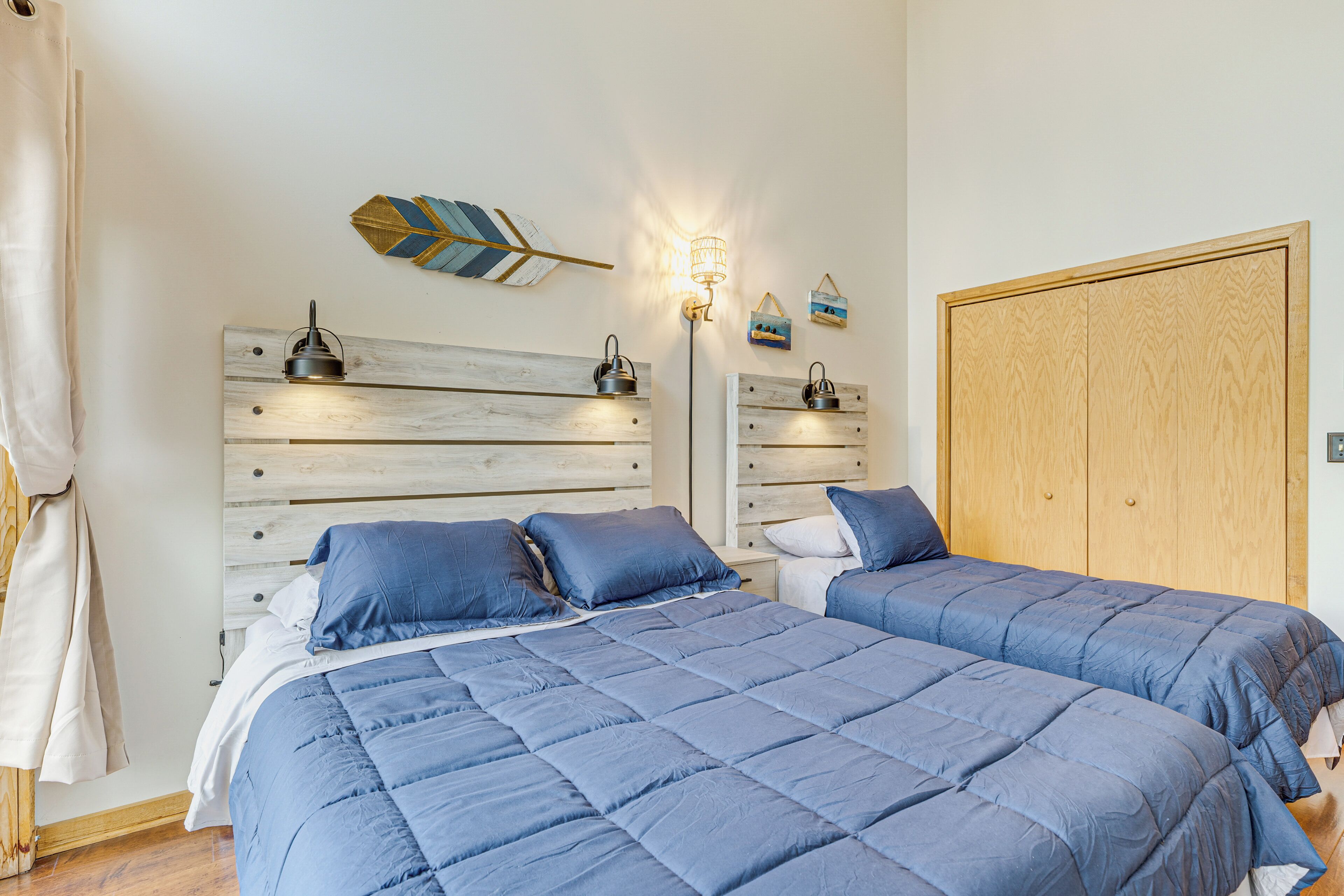 A bedroom with two beds, a wooden headboard, a wardrobe, and wall-mounted lamps.