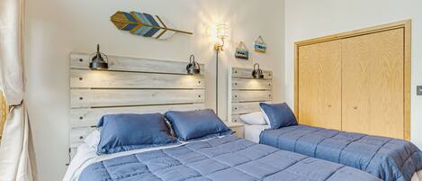 A bedroom with two beds, a wooden headboard, a wardrobe, and wall-mounted lamps.