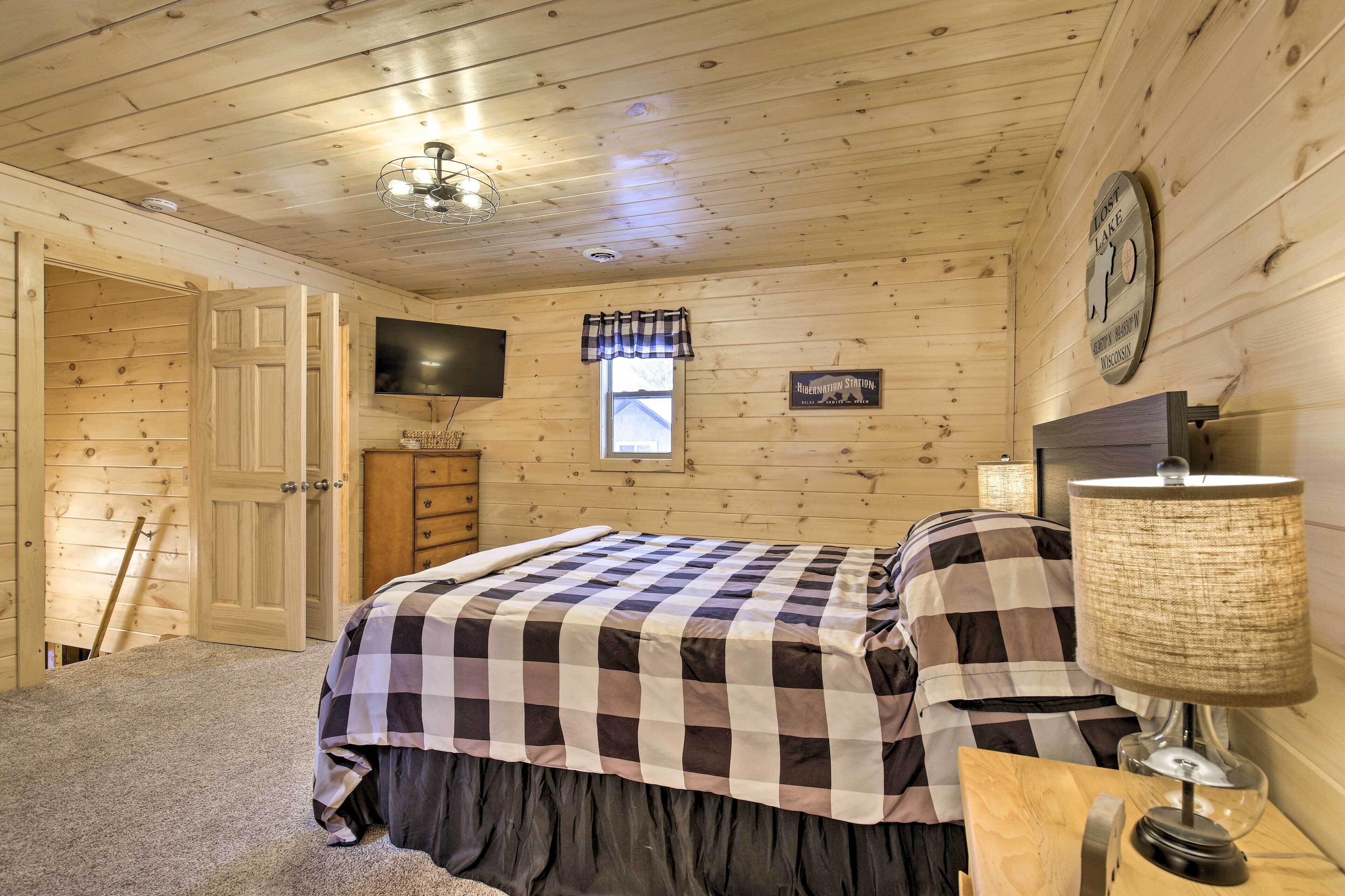Un dormitorio con paneles de madera, una cama, un televisor, una ventana y un reloj en la pared.