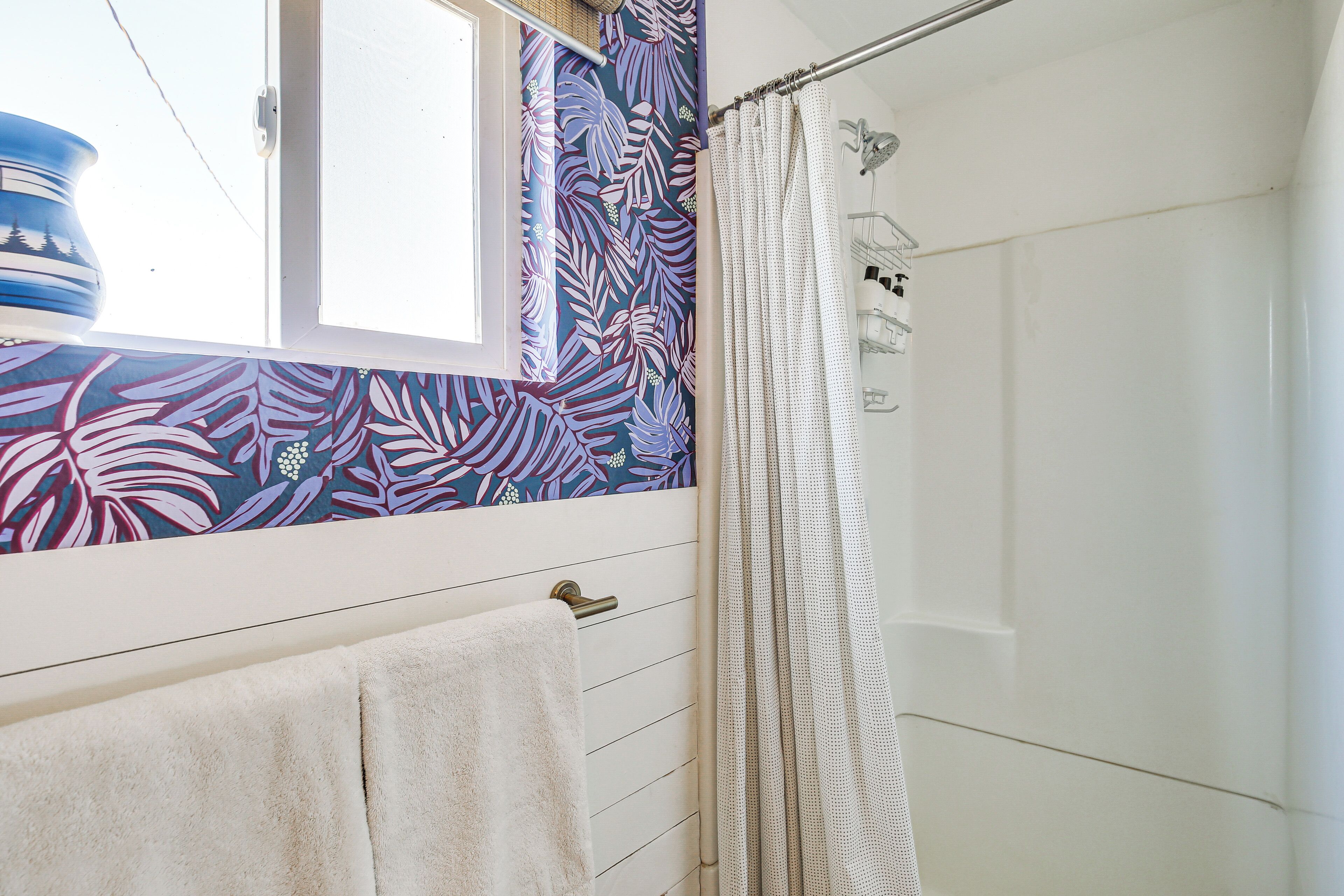 A bathroom with a shower, a towel rack, and a window with a view of the outdoors.