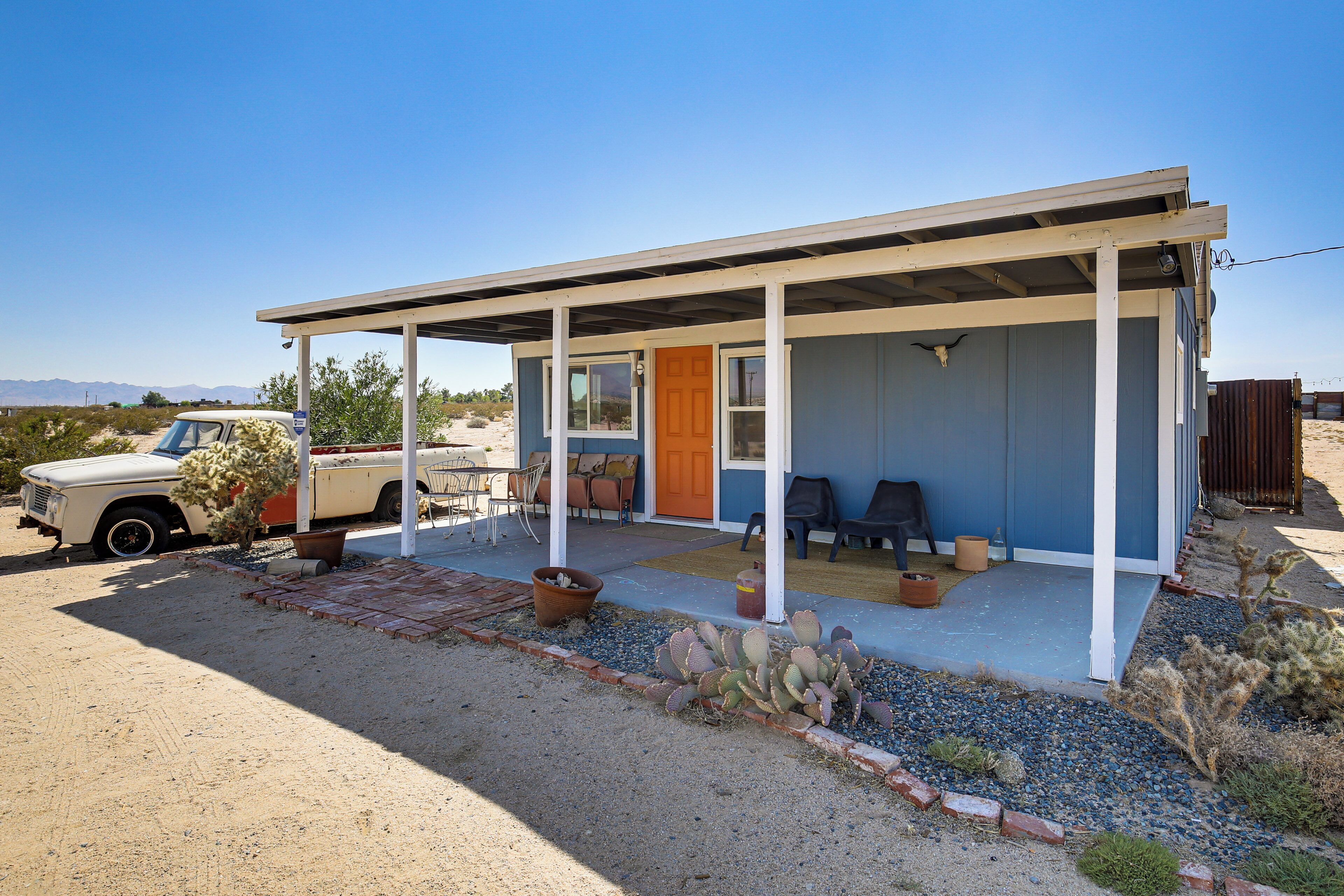 A small, single-story building with a covered porch, a car parked in front, and desert vegetation.