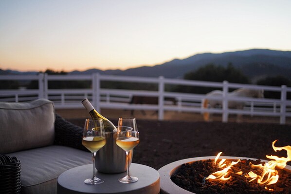 A patio with a white fence, a fire pit, and two glasses of white wine.