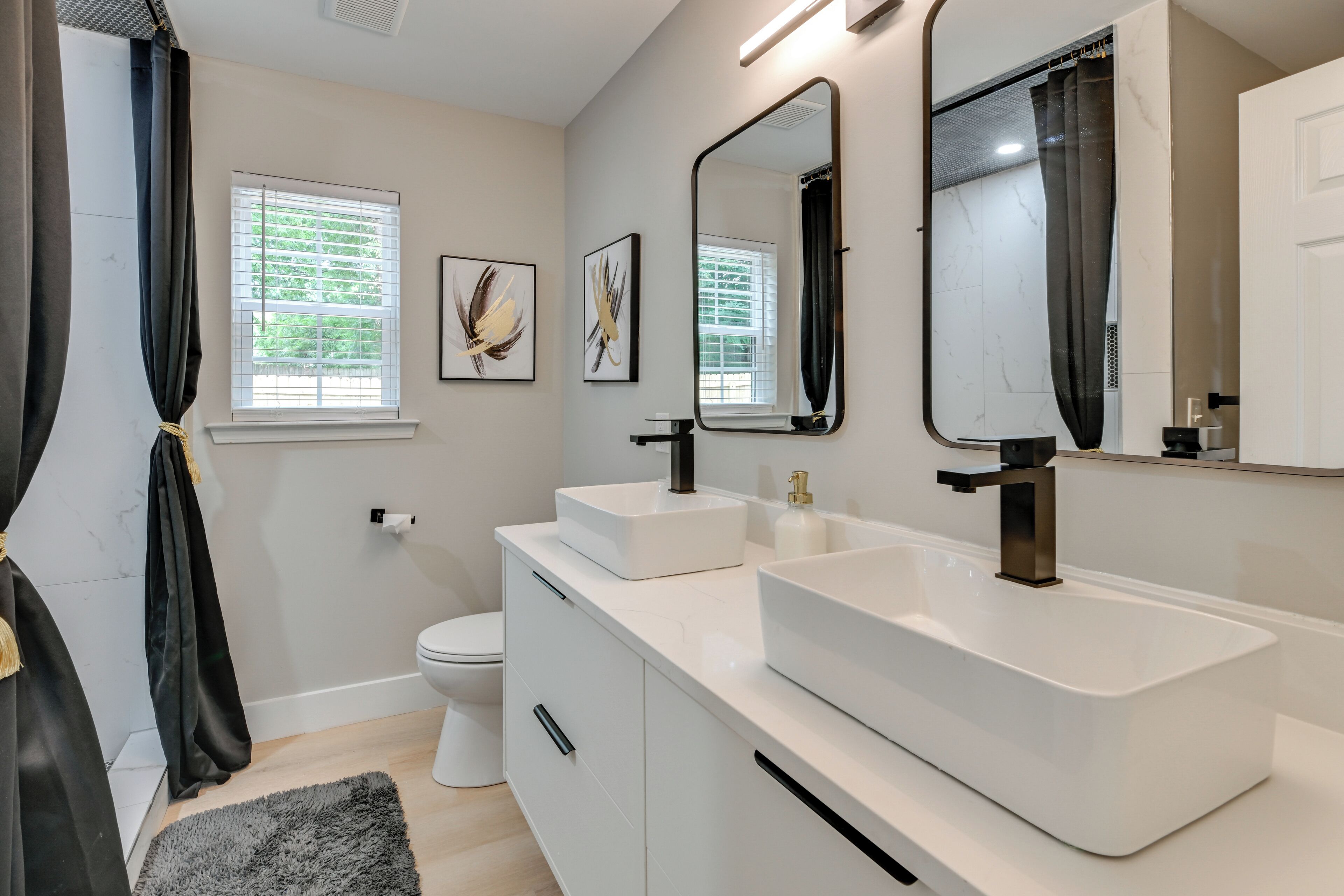 Une salle de bain moderne avec un meuble-lavabo blanc, deux vasques, des toilettes et un grand miroir.