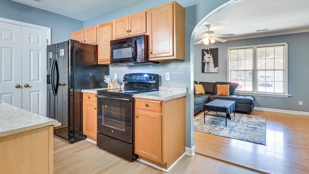 Una cocina moderna con armarios de madera, un refrigerador negro y un microondas. Hay una zona de comedor con un sofá y una alfombra.