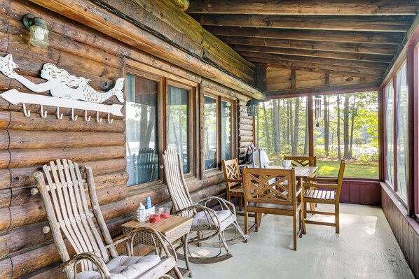 Una cabaña de troncos con un porche, muebles de madera y vistas al bosque.