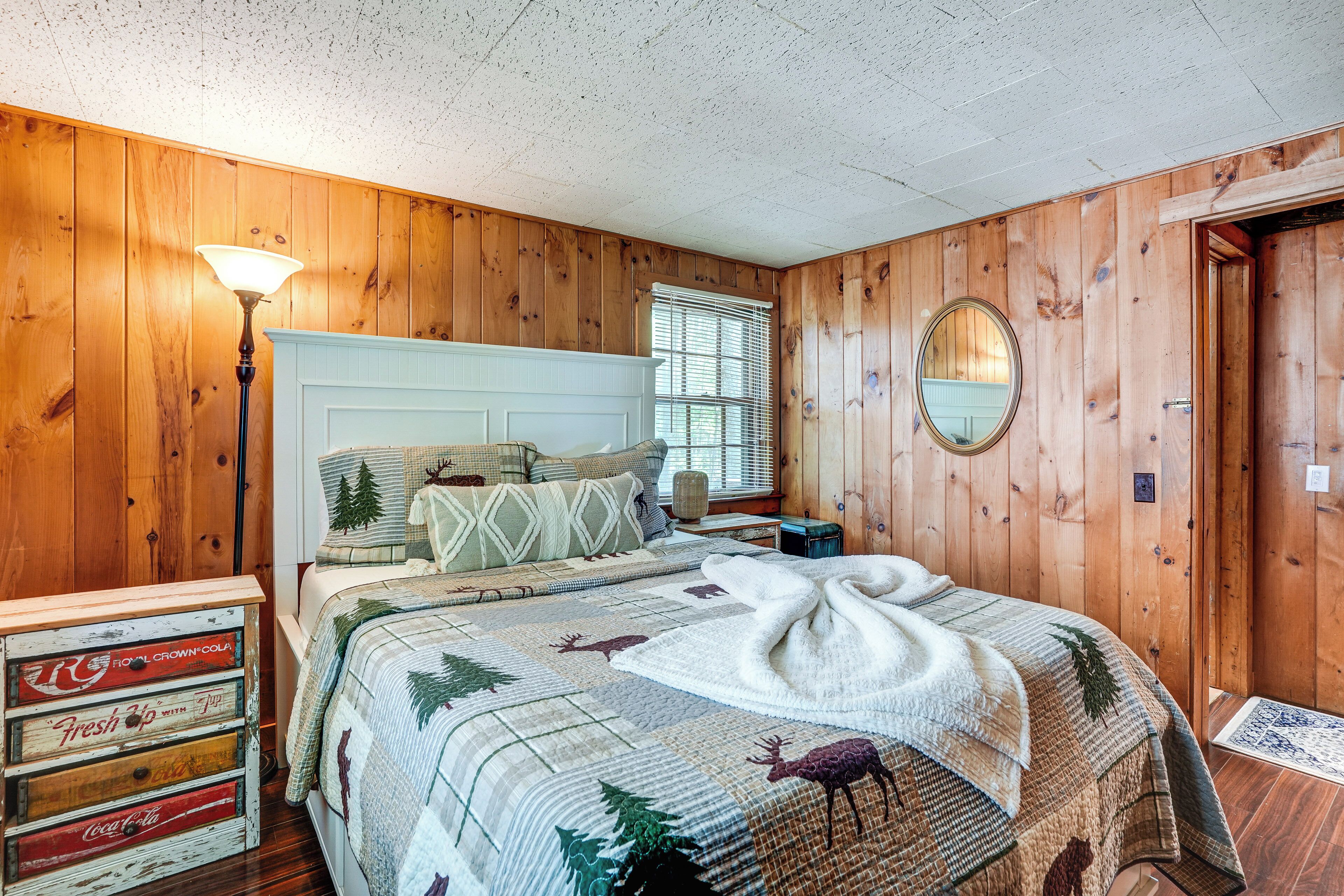 Un dormitorio con paneles de madera, una cama, una mesita de noche, una lámpara y un espejo.