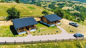 A wooden cabin with a porch and a car parked nearby, surrounded by a rural landscape with hills and a clear sky. - Sub Stele Chalets (Holbav)