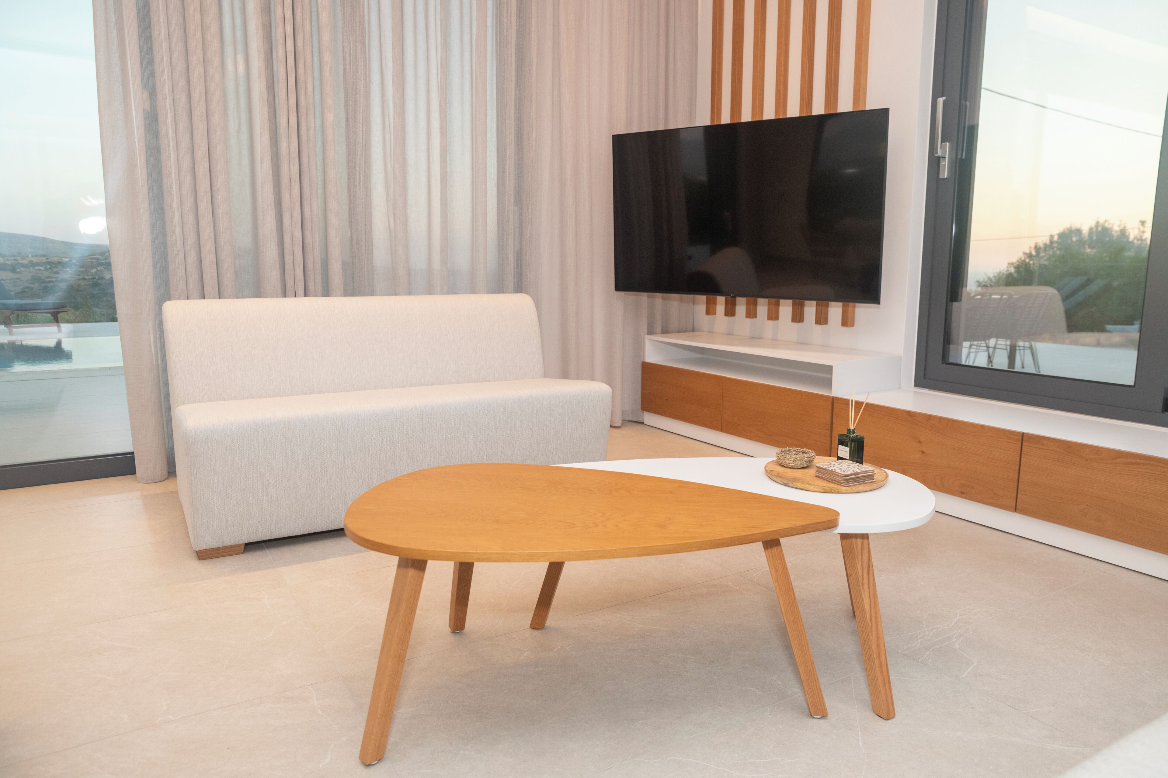 A modern living room with a white sofa, a wooden coffee table, and a flat-screen TV mounted on a wooden cabinet.