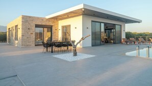 A modern house with a pool, stone walls, and a dining area with outdoor furniture. - Antiope Retreat (Pitsidia)