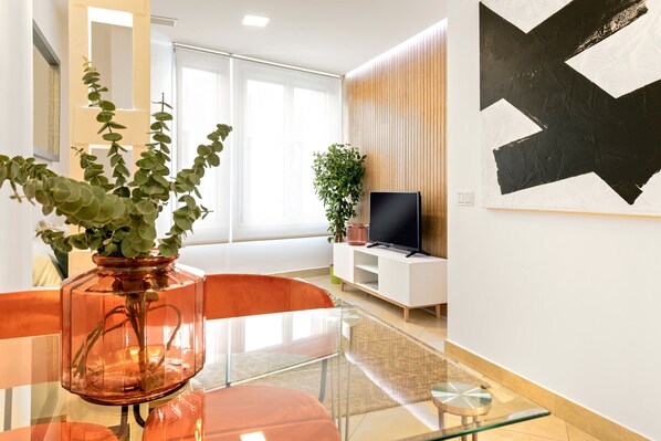 A modern living room with a glass dining table, a red chair, a potted plant, a flat-screen TV, and a large abstract painting on the wall. - Luminous 1 Bedroom Apartment in the Heart of Seville. Murillo V (Seville)
