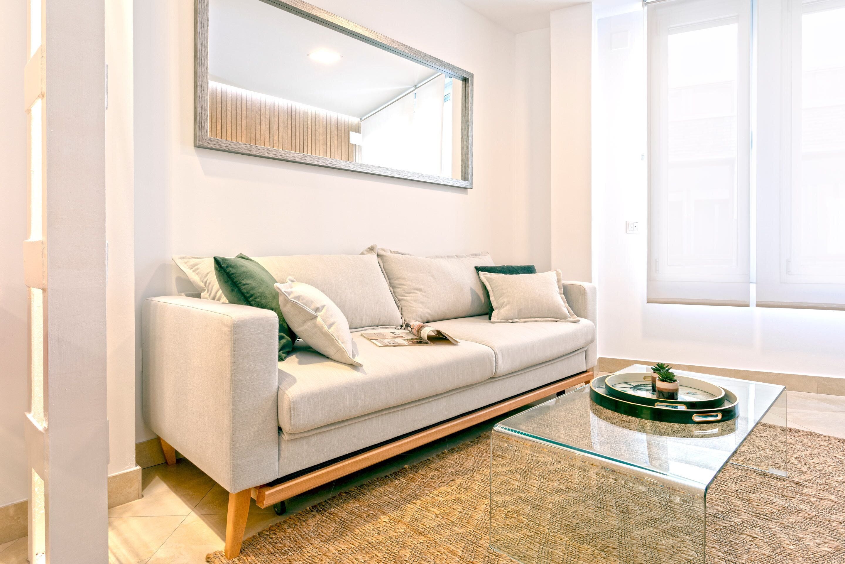 Uma sala de estar moderna com um sofá, uma mesa de centro de vidro e um espelho grande na parede.